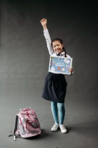 Okula başlayan, sırt çantalı ve 'Back to School' tabelası tutan mutlu bir çocuk elini kaldırıyor